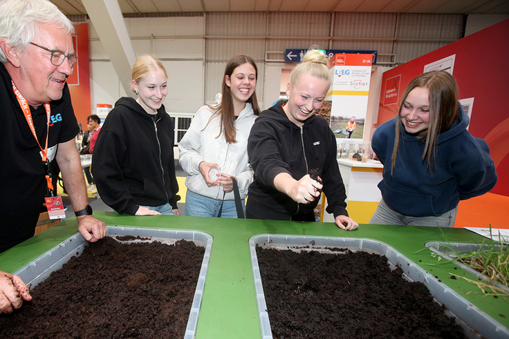 Wie gut speichert Schwarztorf im Gegensatz zu Weißtorf Wasser? LBEG-Bodenexperte Uwe Hammerschmidt (li.) lässt das die Messestand-Besucherinnen am Moorpodest ausprobieren.