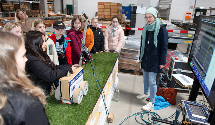 Mit dem Georadar gehen die Schülerinnen und Schüler auf Schatzsuche und sehen über den Bildschirm rechts, ob sich etwas unter dem grünen Teppich verbirgt.