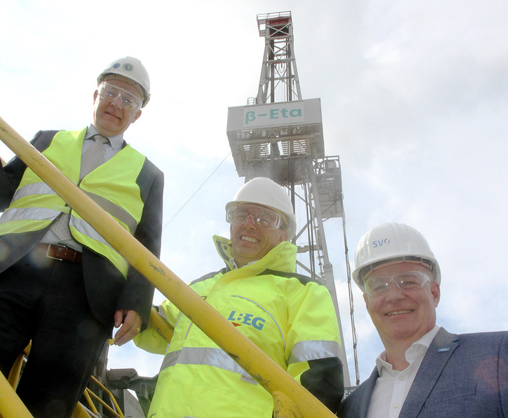 Das Bild zeigt drei Personen: Sven Krueger, Geschäftsführer von Baker Hughes, LBEG-Präsident Carsten Mühlenmeier und SVO-Geschäftsführer Holger Schwenke (v.li.), die vor einem Bohrturm stehen.
