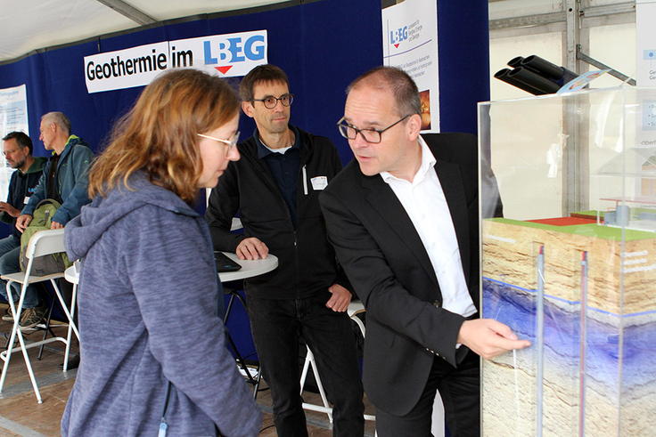 Das Foto zeigt von links eine Expertin und einen Experten, die an einem Schaumodell Niedersachsens Wirtschaftsminister Grant Hendrik Tonne verschiedene Möglichkeiten der Erdwärmegewinnung zeigen.