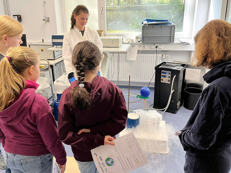 Das Bild zeigt Schülerinnen und Schüler, die sich einen brodelnden Topf anschauen.