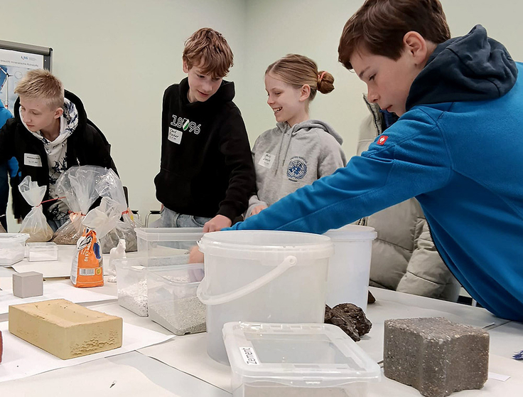 Das Bild zeigt Schülerinnen und Schüler, die Rohstoffproben anfassen und testen.